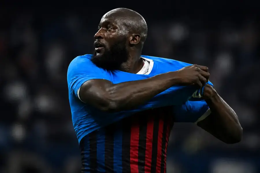 Lukaku si toglie la maglia del Napoli e sotto si intravede metà maglia Inter e metà maglia Milan, immagine creata con intelligenza artificiale