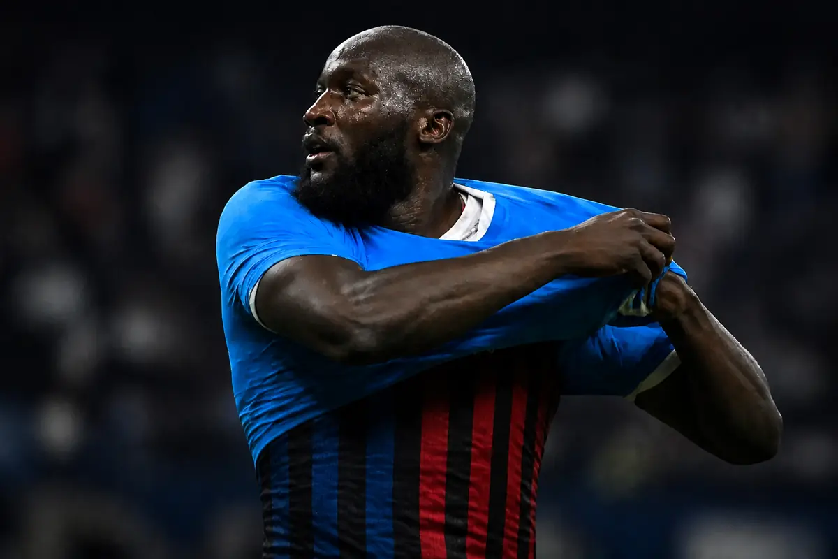 Lukaku si toglie la maglia del Napoli e sotto si intravede metà maglia Inter e metà maglia Milan, immagine creata con intelligenza artificiale