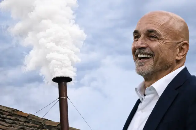 Luciano Spalletti sorridente con un comignolo da cui esce una fumata bianca